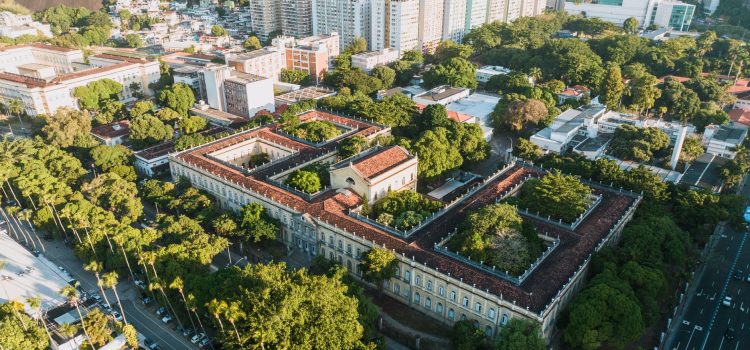 Vista aérea de um campus universitário histórico, cercado por áreas verdes, no Rio de Janeiro.