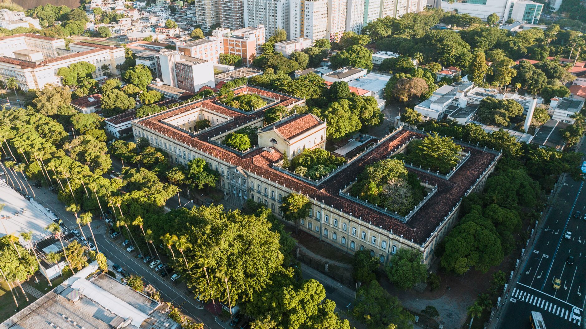 Vista aérea de um campus universitário histórico, cercado por áreas verdes, no Rio de Janeiro.