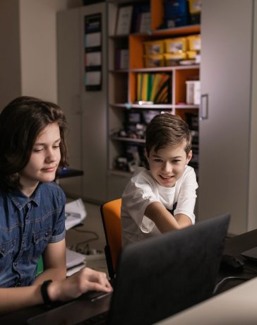 Estudantes usam laptops em sala de aula enquanto um professor acompanha a atividade.