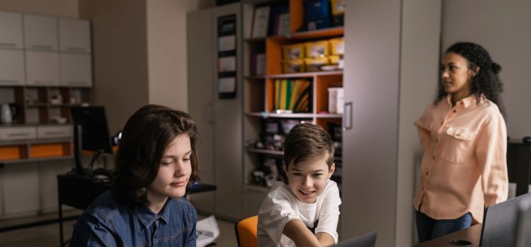 Estudantes usam laptops em sala de aula enquanto um professor acompanha a atividade.