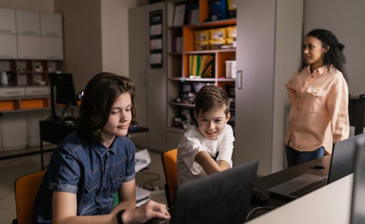 Estudantes usam laptops em sala de aula enquanto um professor acompanha a atividade.