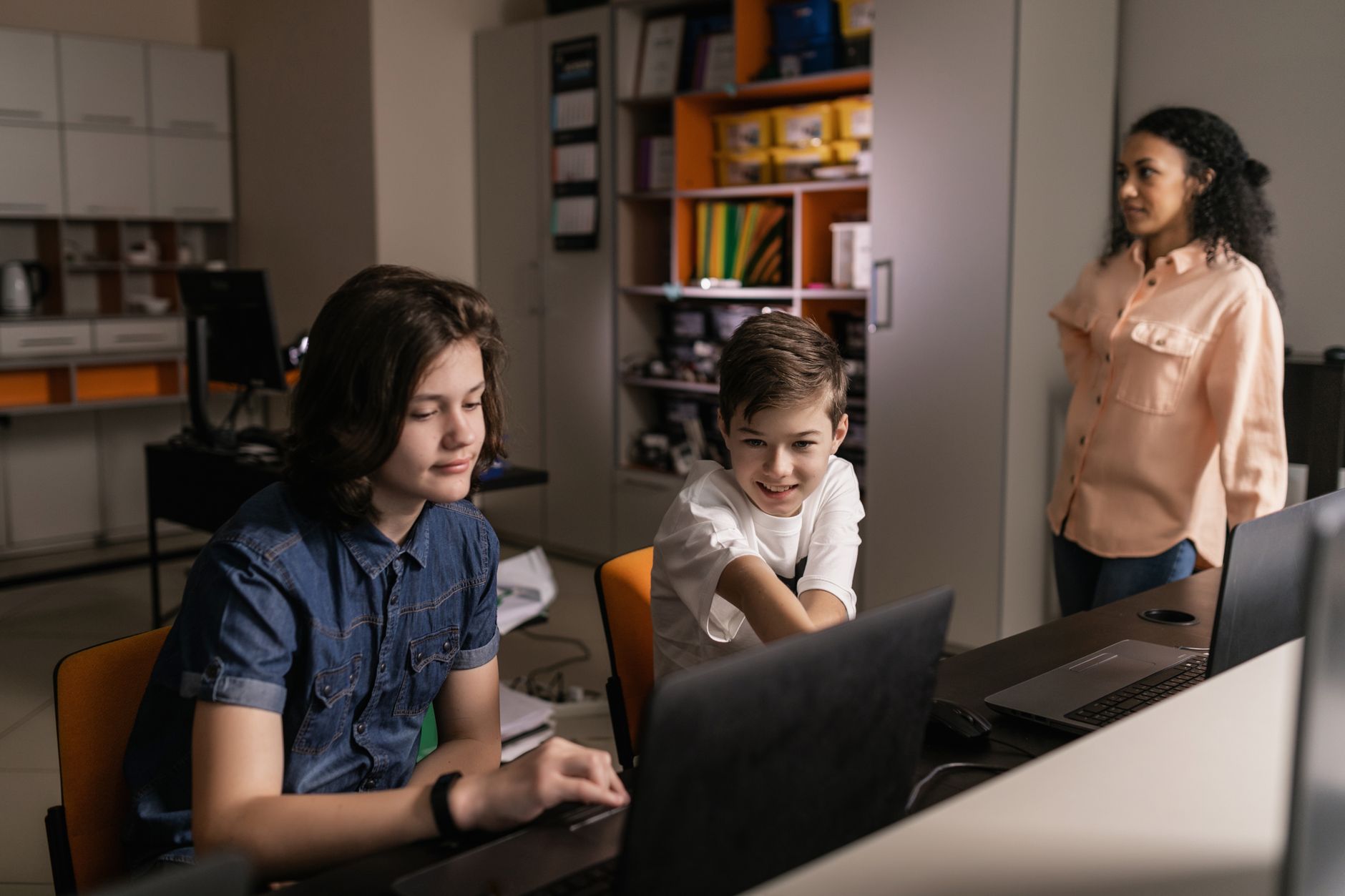 Estudantes usam laptops em sala de aula enquanto um professor acompanha a atividade.