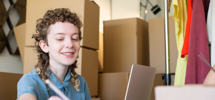 Empreendedora sorridente trabalha com um laptop enquanto organiza pacotes de sua pequena empresa.