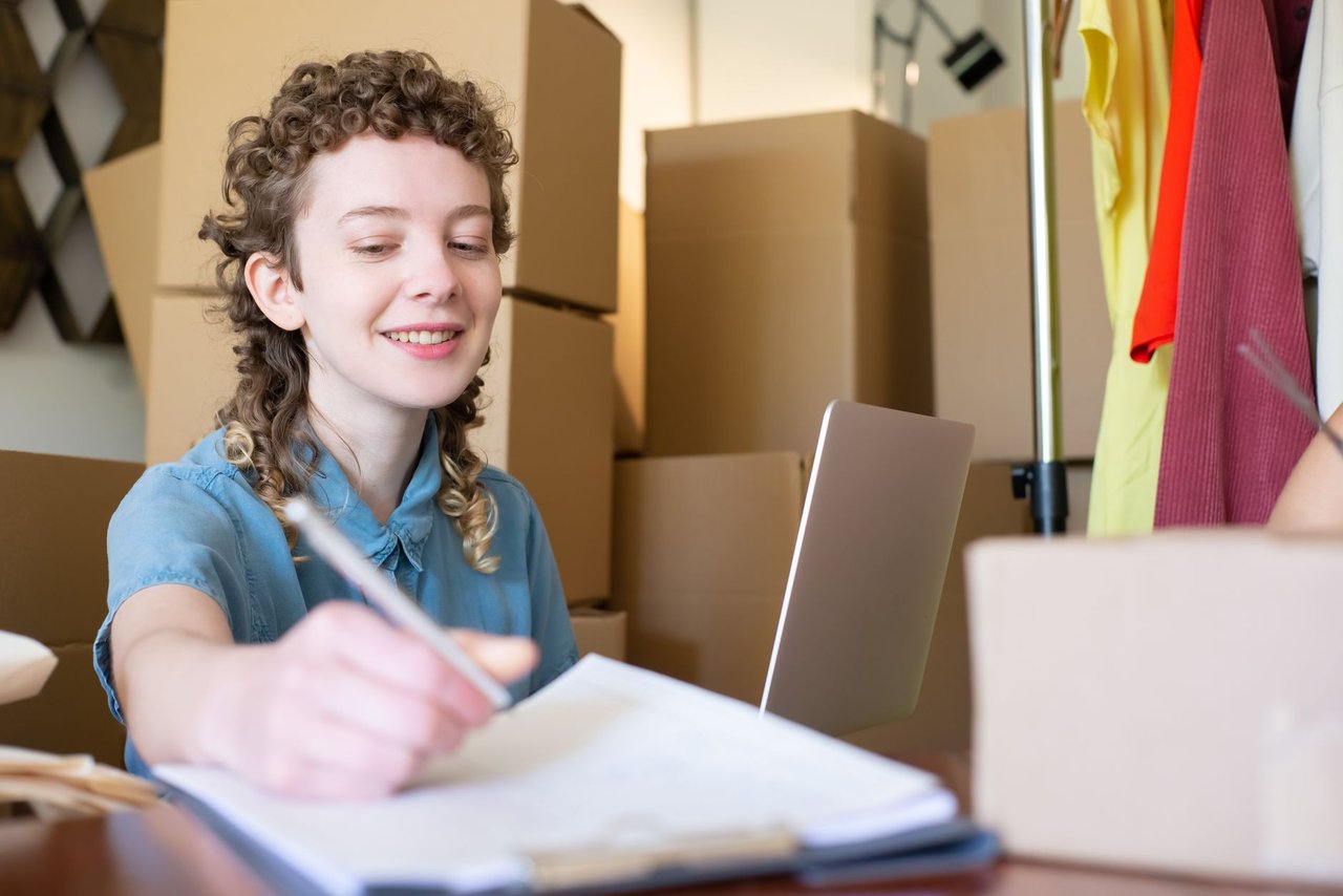 Empreendedora sorridente trabalha com um laptop enquanto organiza pacotes de sua pequena empresa.