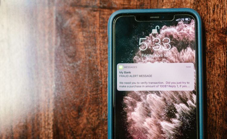 Smartphone exibindo uma notificação de alerta contra fraude sobre uma superfície de madeira.